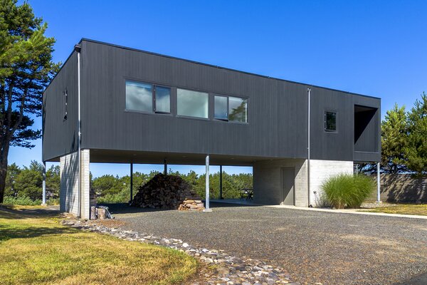 The home's perched positioning creates ample covered outdoor space, including room for parking. Tall trees surround the property, presenting a private, peaceful oasis.