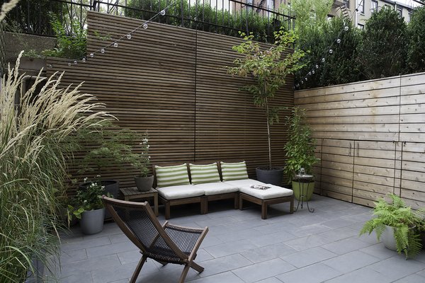 The living room leads to a private outdoor patio. Before the renovation, the slightly below grade area was in plain sight to passersby, as it lays adjacent to the public walkway into the building. This less-than-ideal setup was addressed in the redesign by adding a slatted cedar perimeter fence, along with tall trees and shrubs. Clever hidden doors conceal patio storage under the entry walkway.