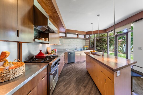 The airy kitchen is fitted with black walnut cabinetry, stainless steel countertops, and a six-burner Viking Range. Floor-to-ceiling windows connect the space to the private backyard.