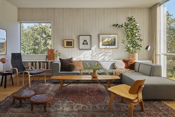 A BoConcept sectional is joined by a  Yngve Ekström lounge chair and ottoman and an Eames chair in the living area. The couple found the vintage Danish coffee table at a flea market, while the traditional Indian stools were purchased for their wedding. Whitewashed poplar clads the far wall.