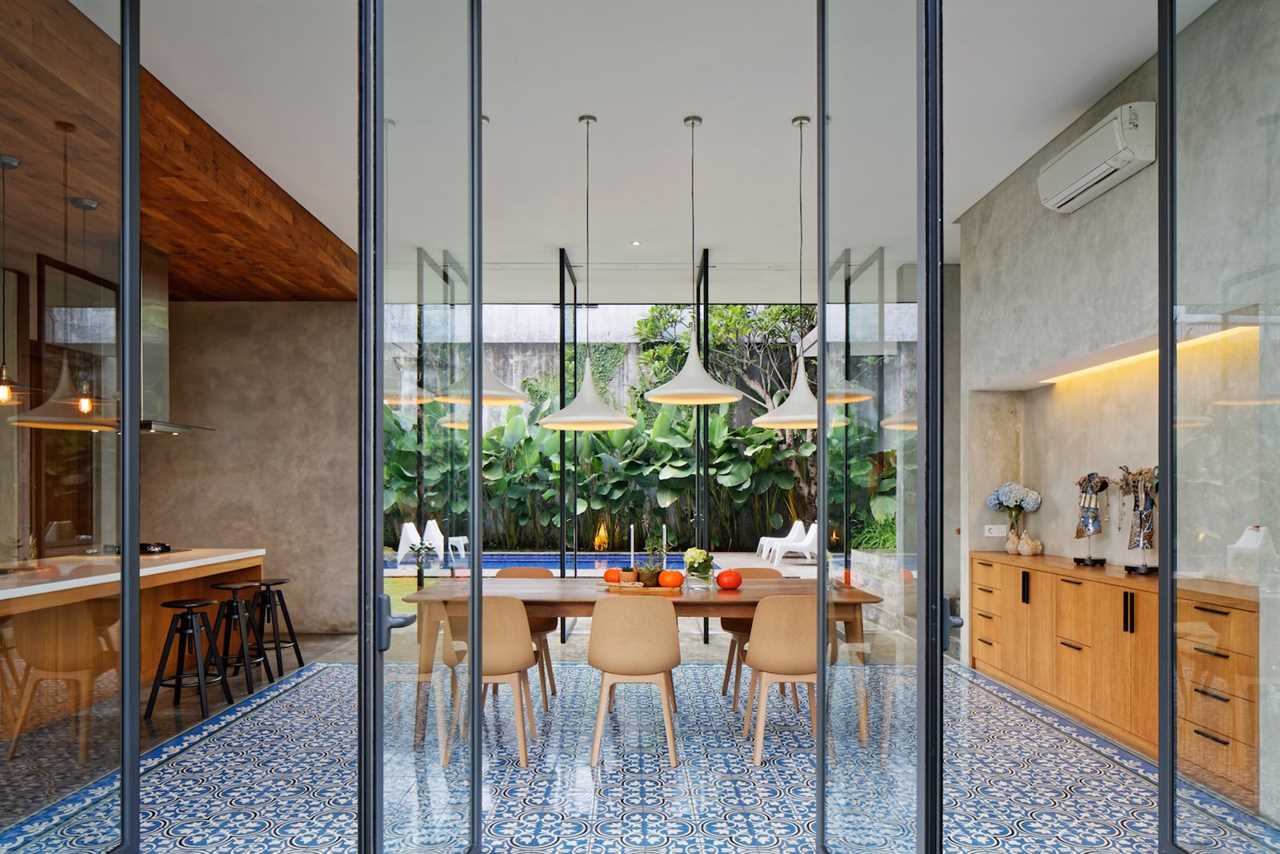 An old mango tree, welcoming visitors to the grounds, inspired the arrangement of this Semarang home designed by architect Tamara Wibowo for her family of five. Three volumes—living, service, and office and garage—are clad in concrete to alleviate solar gain and maximize cross-breezes through large openings lined with teak. Floor-to-ceiling glass opens the dining room, marked by geometric Tegel Kunci tiles, onto greenery.