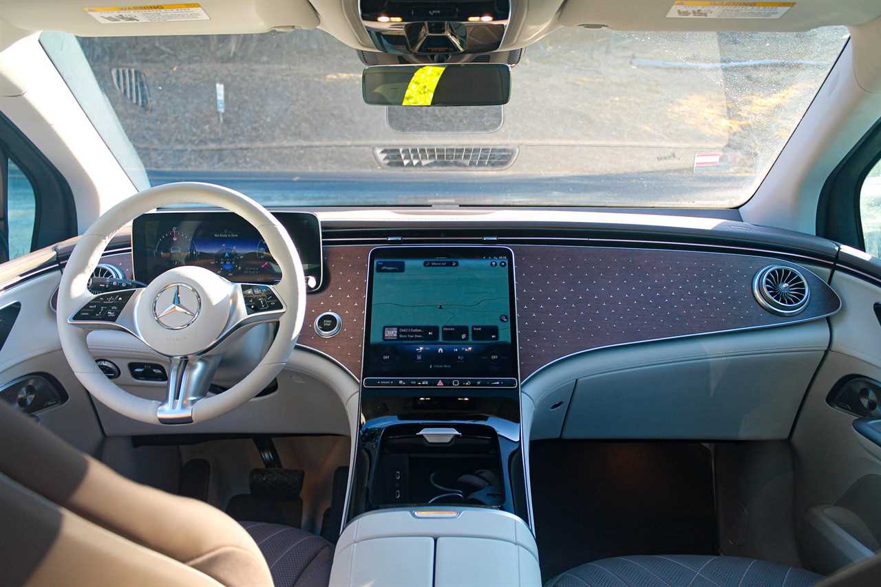 The dashboard of the 2023 Mercedes-Benz EQE SUV electric car, featuring a white steering wheel and wood accents. 