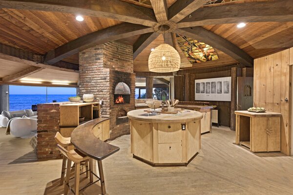 The kitchen, located steps from the main living area, comes with a circular island, fireplace, tile countertops, and stained-glass lunettes fitted into the beams overhead.