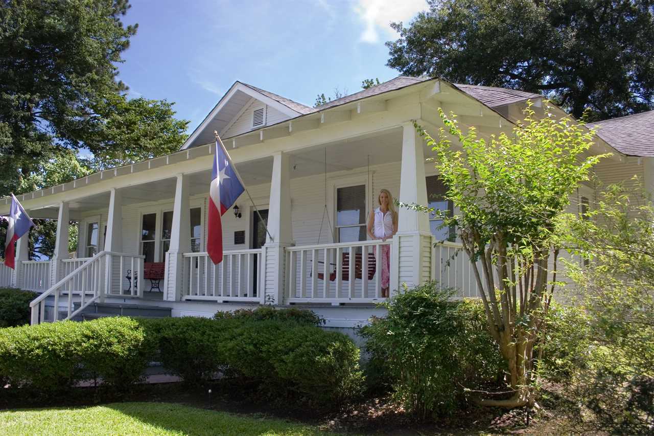 A woman standing in front of a home with the Texas flag.