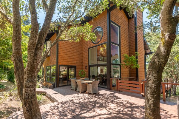 The wood-clad home sits on a lush lot surrounded by shady trees, offering a peaceful oasis.