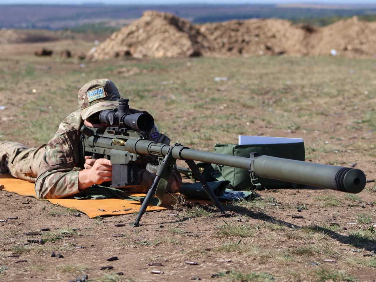 A Ukrainian sniper lies on the ground looking through the sight of the rifle.