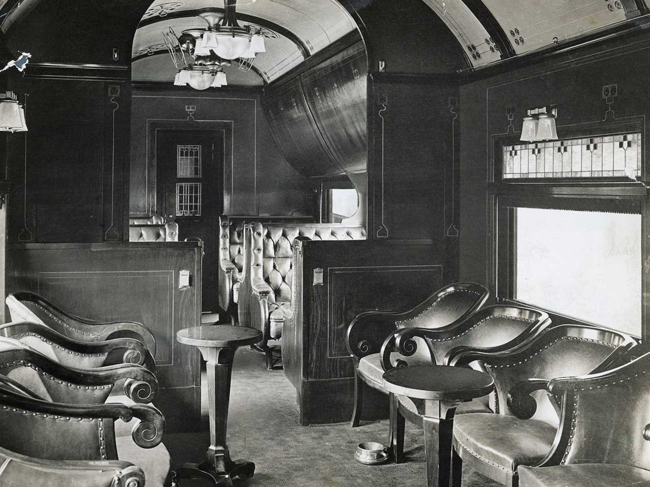 The interior of a 19th century luxury buffet rail car with several leather chairs, bench seats, and chandeliers