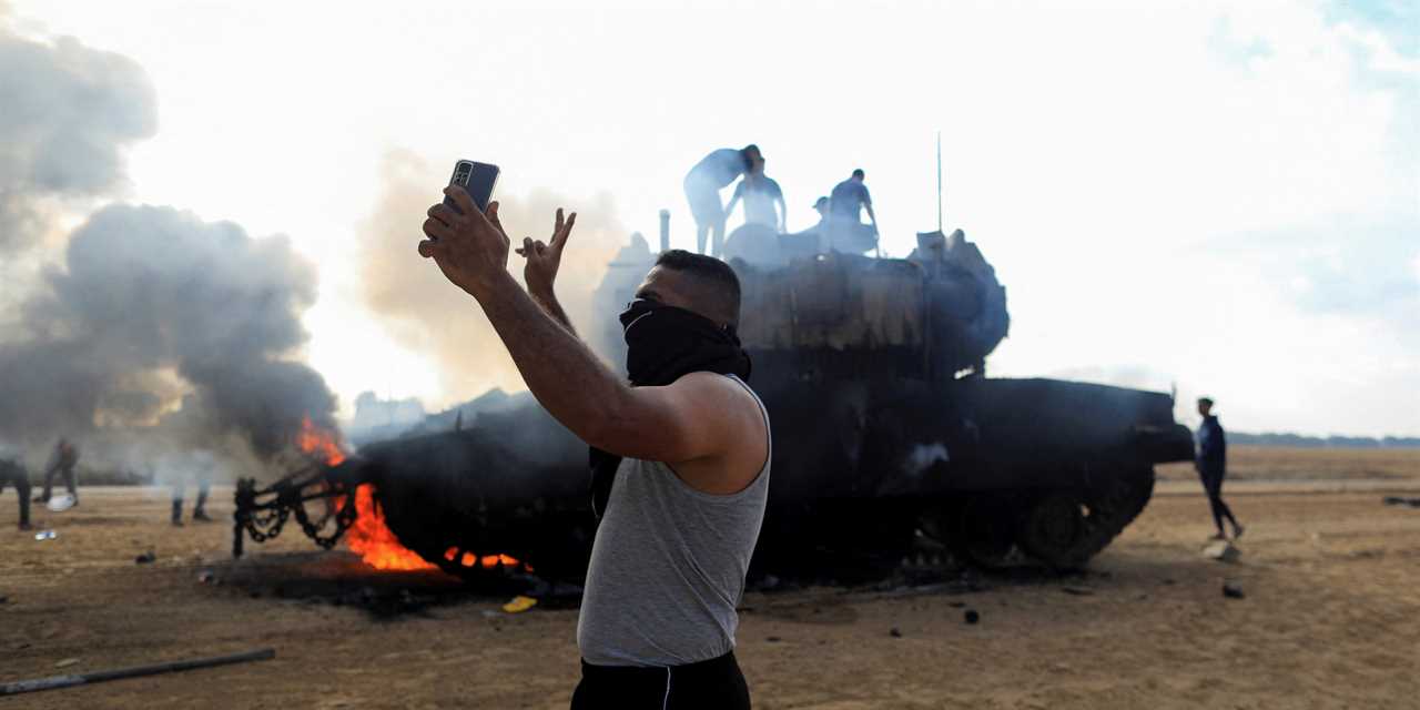 A Palestinian man takes a selfie in front of a burning Israeli military vehicle after it was hit by Palestinian gunmen who infiltrated areas of southern Israel, at the Israeli side of Israel-Gaza border.