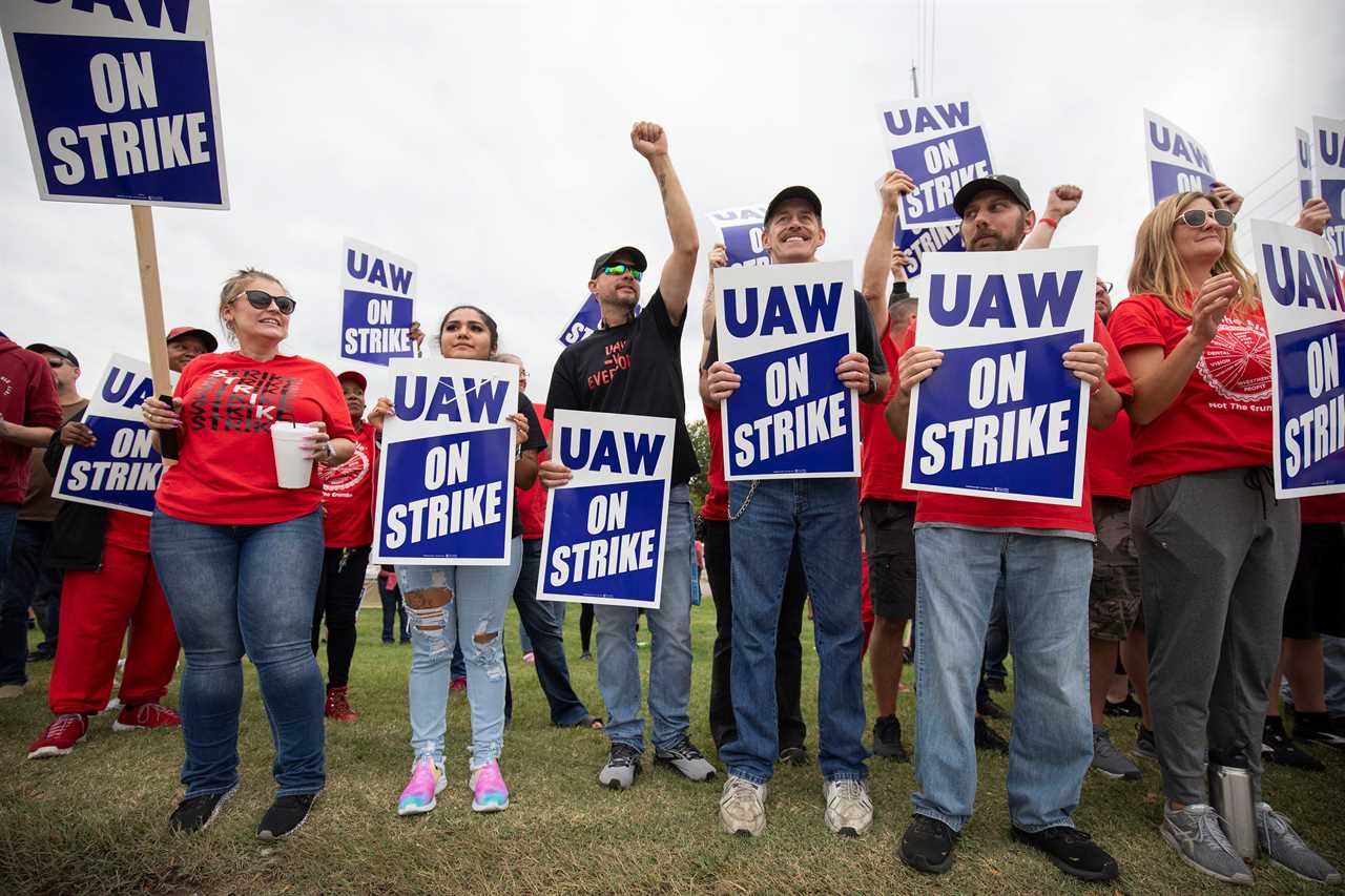 Union members in red t-shirts carrying blue UAW signs stand on strike.