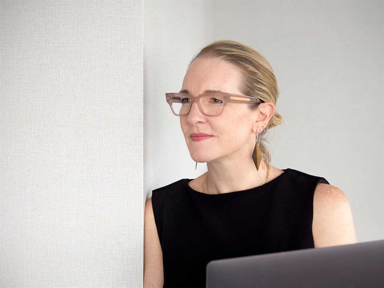 Headshot of Erin Derby in front of a computer looking to the left, wearing a black top and gold earrings.