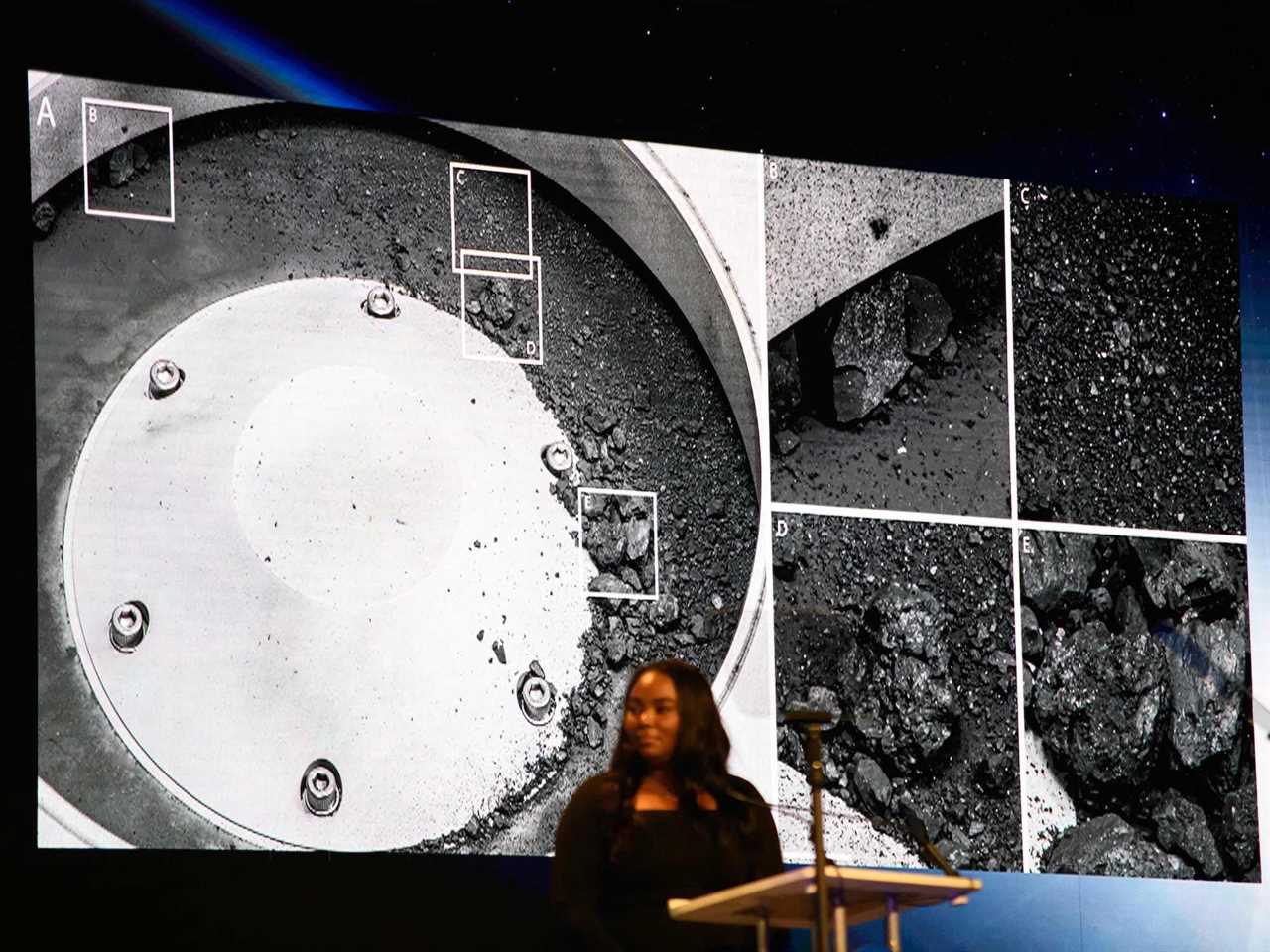 A woman stands in front of a large screen displaying images from the asteroid Bennu at a NASA press conference