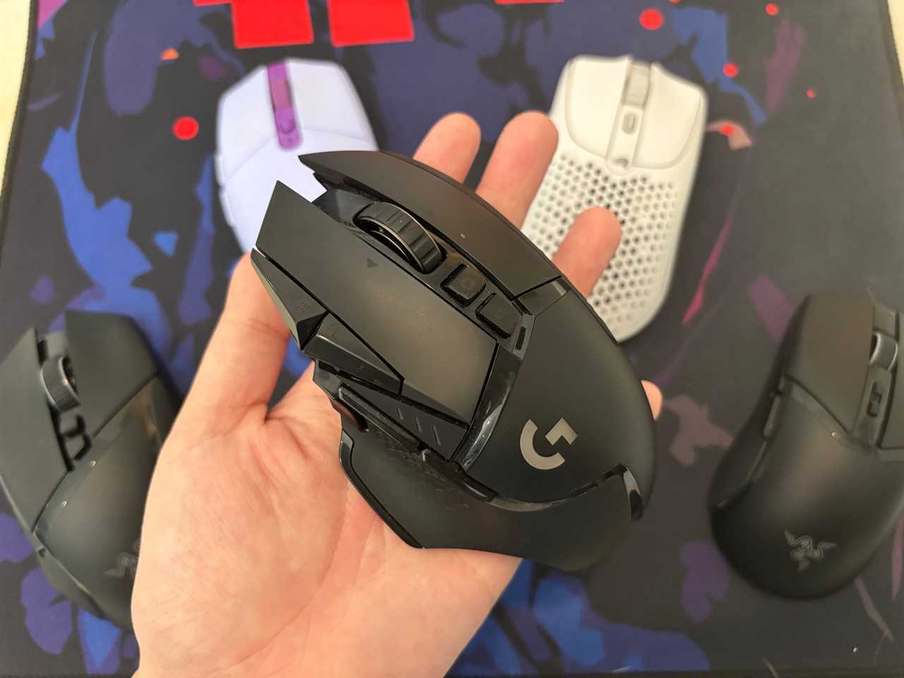 the logitech g502 lightspeed held in a hand in front of other wireless gaming mice