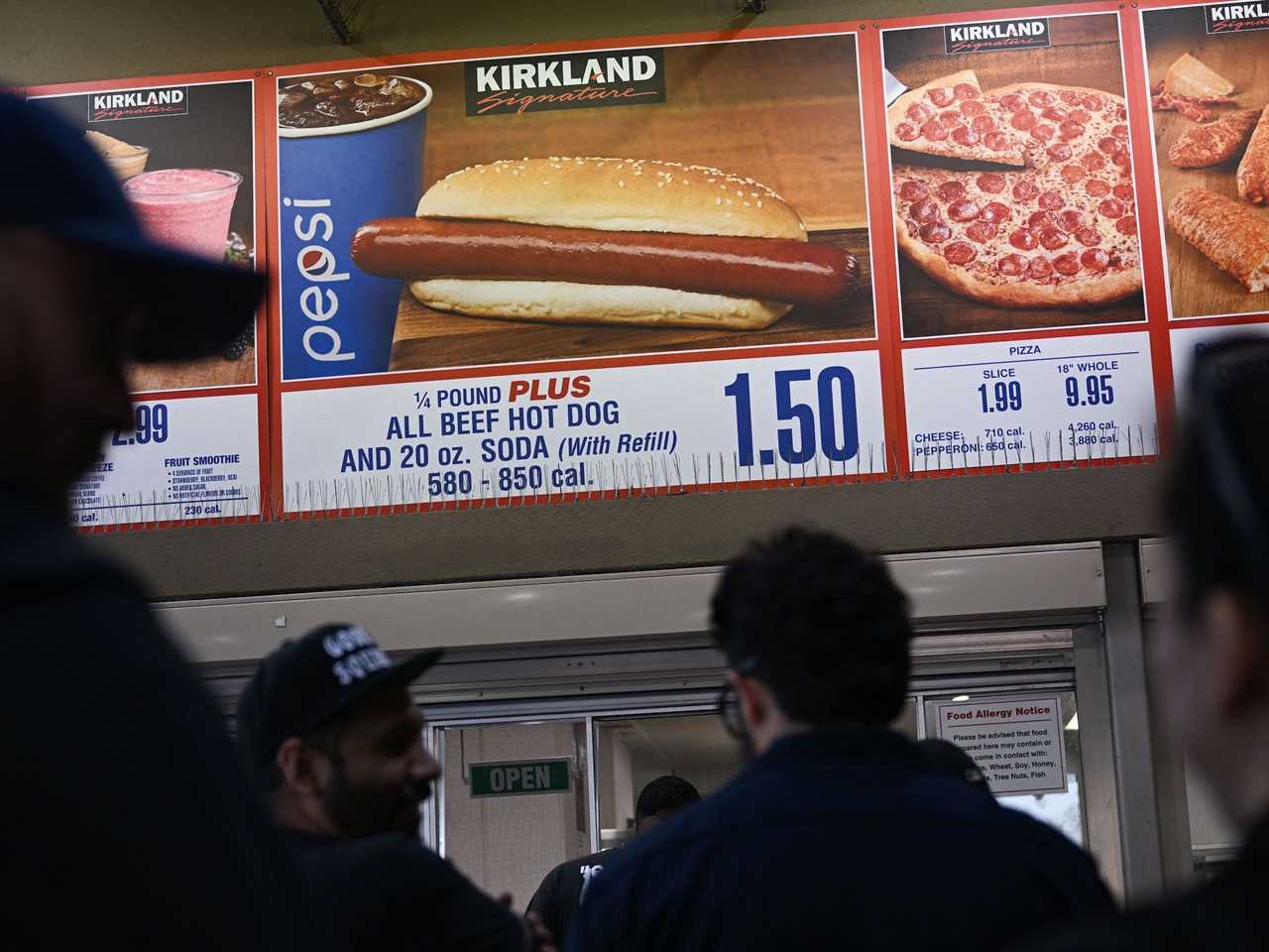 Customers wait in line for Costco hot dog with sign showing the hot dog visible over their heads