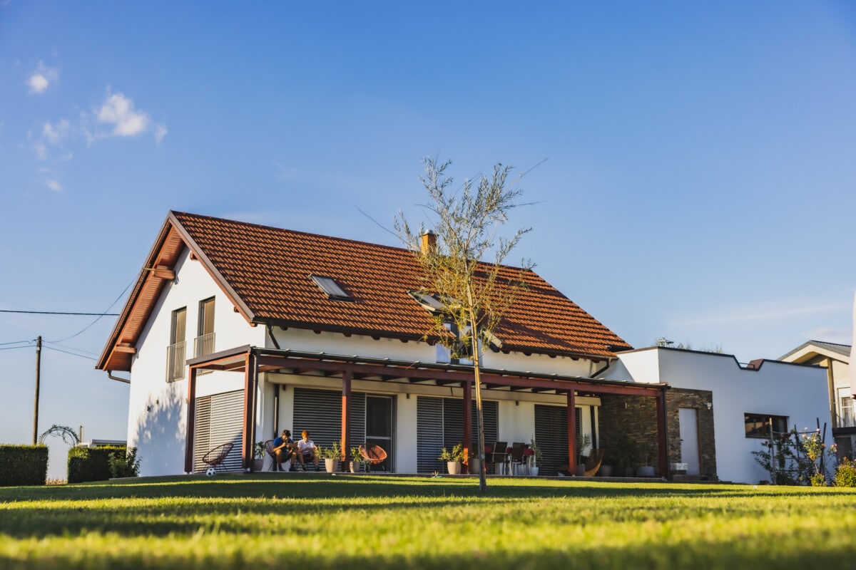 Modern house with terrace on the countryside,two boys sitting on chairs on the terrace and using their phone,clear sky in the background