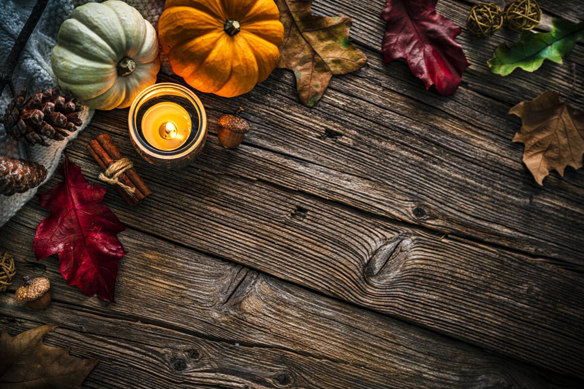 Autumn or Thanksgiving decoration: overhead view of gourds, dry leaves, burning candle, cinnamon sticks, pine cones shot on rustic wooden table. 