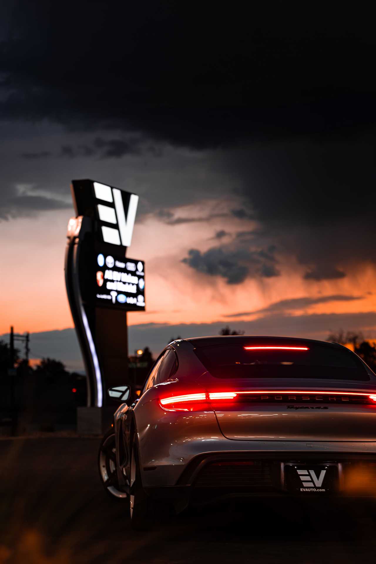 A Porsche EV is parked in front of a dealership sign in the dark.