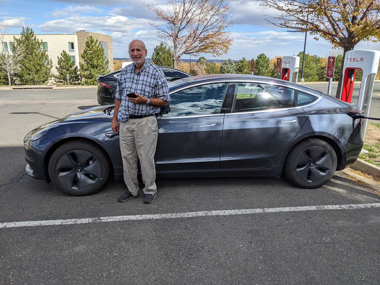 A man stands in front of a Tesla EV charging at a Tesla charger.