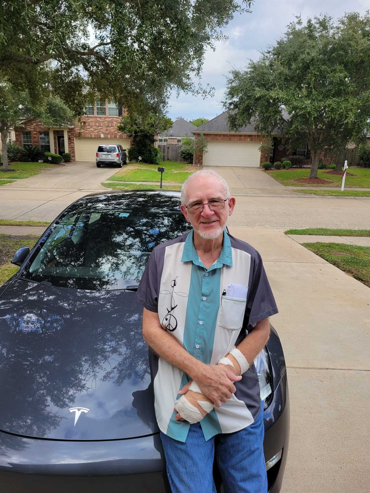 A man stands in front of his Tesla in a driveway.