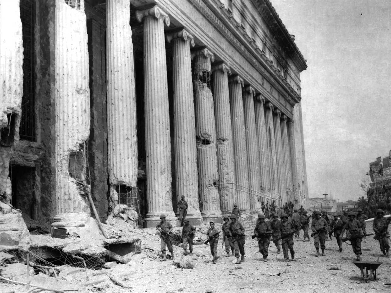 A company of US infantry troops moves past the General Post Office building on their way to assault the walled city of Intramuros Feb. 23, 1945, in Manila, Philippines. The month-long battle laid waste to much of Manila.