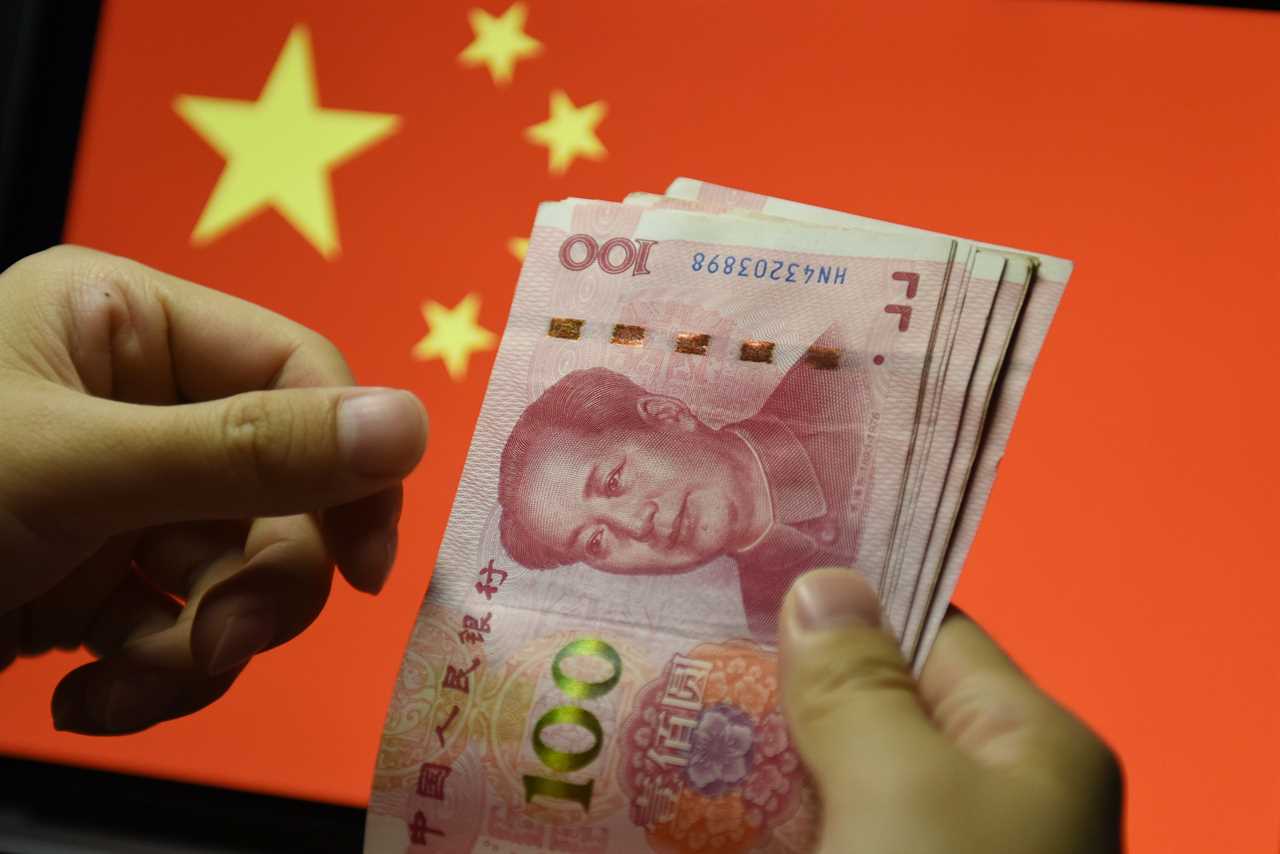 In this photo illustration a man counts 100 RMB notes with the Chinese flag in the background. In recent years, China has clamped down on shadow banking, concerned about the hidden risks in the high volume of complex and potentially risky loans in the sector. As a weakening economy puts pressure on businesses and individuals, authorities fear shadow lending and illegal loans might surge.