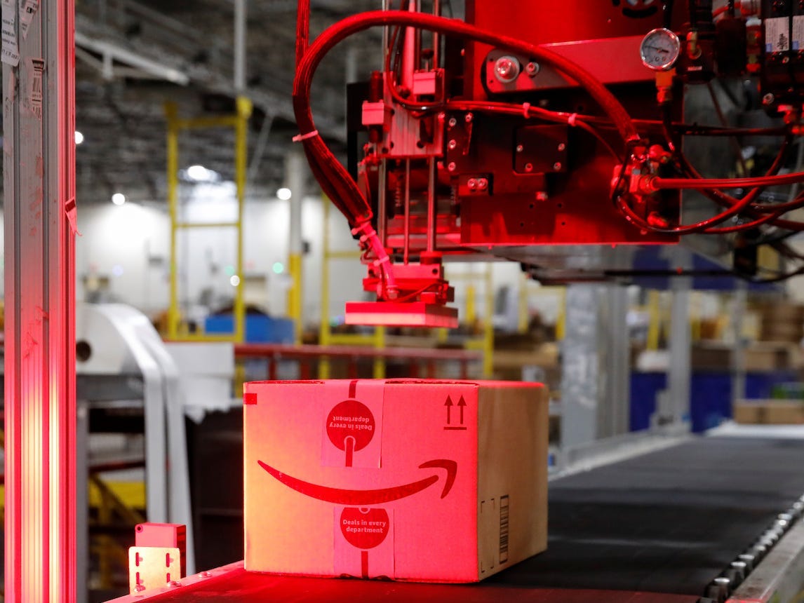 An Amazon box is seen on a conveyer belt below a robotic arm cast in red lighting