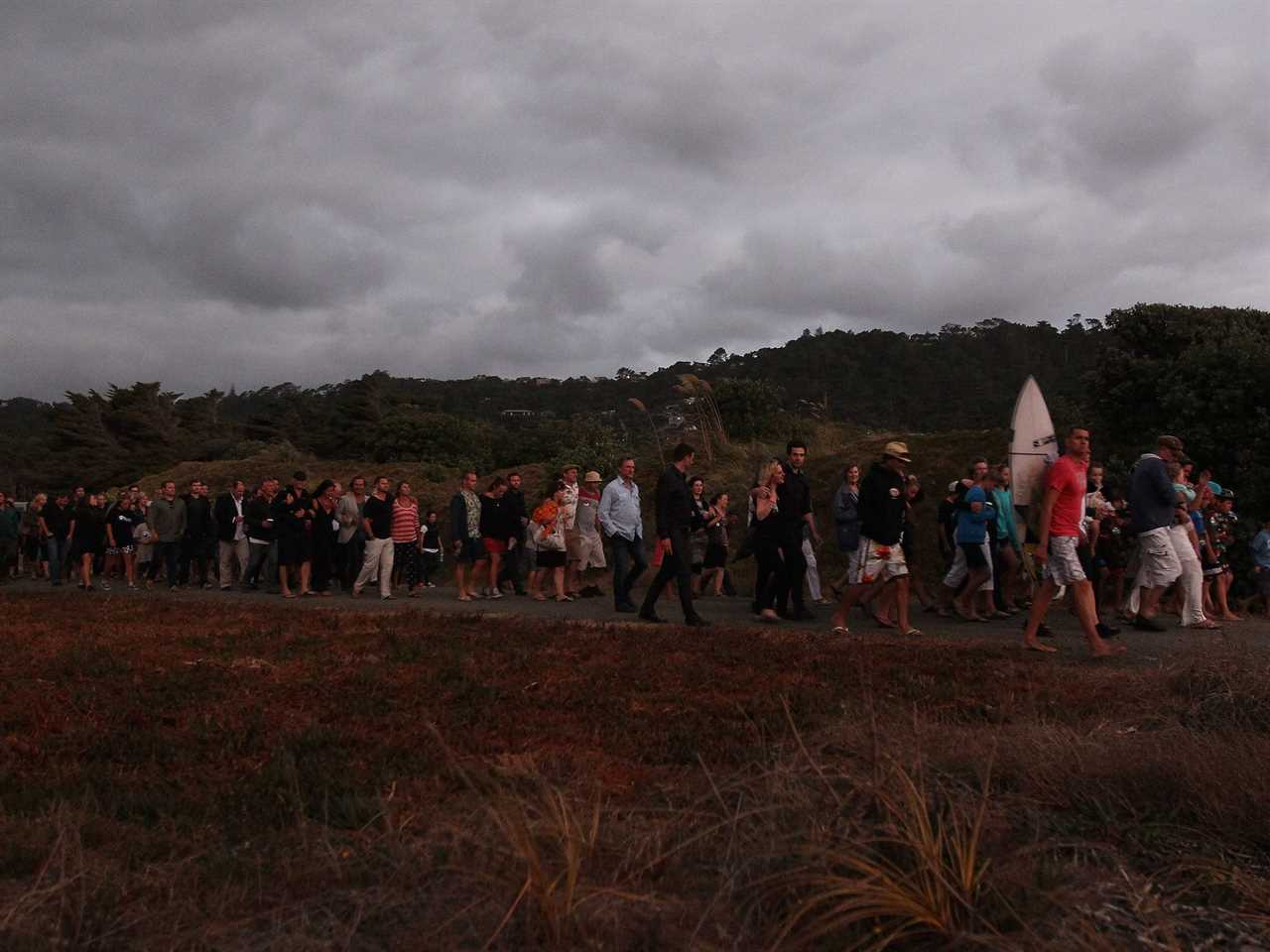 Friends and family of Adam Strange, the victim of a fatal shark attack walk toward Muriwai Beach for a sunset farewell.