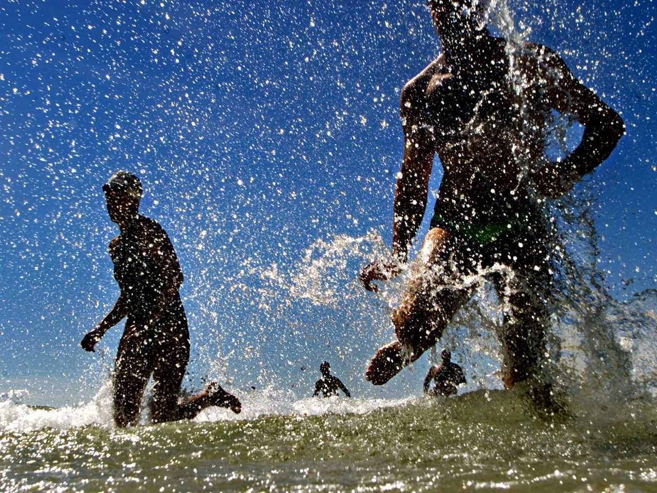 Competitors race on the beach and kick up water droplets.