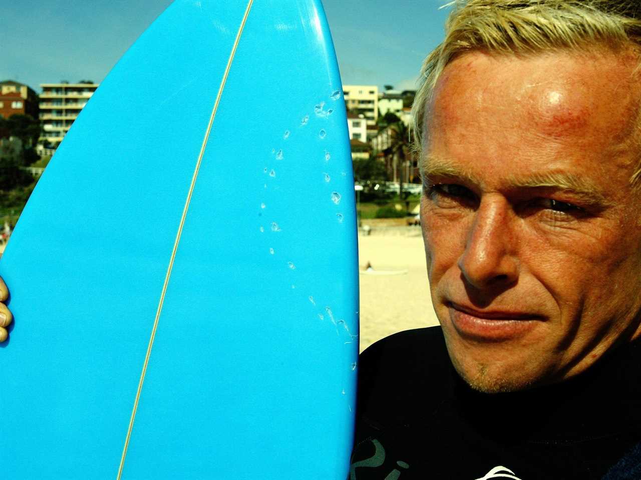 Simon Letch, who was attacked by a shark while surfing, poses for a photo with his board with bite marks from a shark.