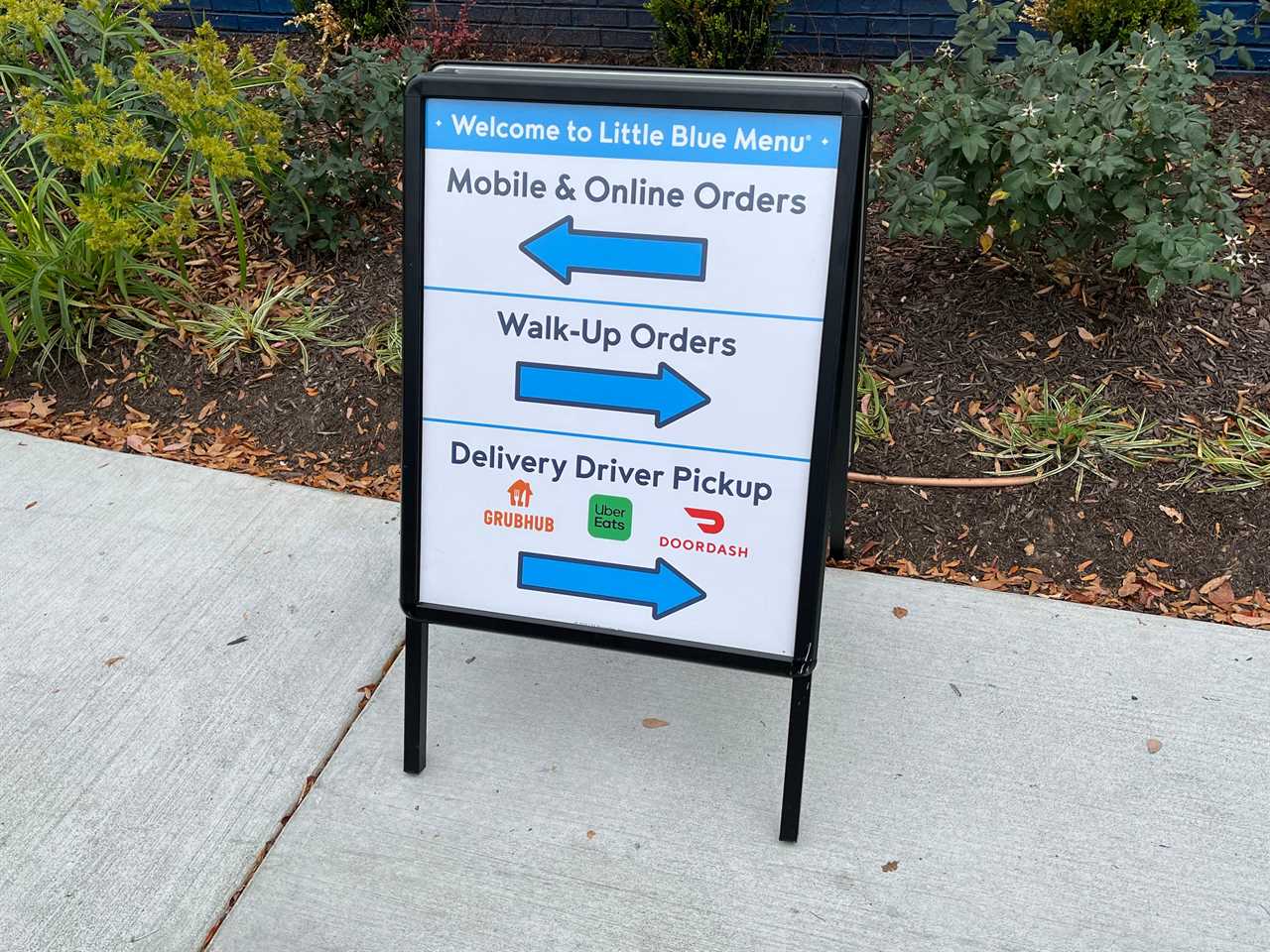 A sign at Little Blue Menu directs diners and delivery drivers to separate windows depending on whether they want to place an order, pick one up that they placed via a mobile app, or pick up an order as a delivery driver for a third-party service like DoorDash.