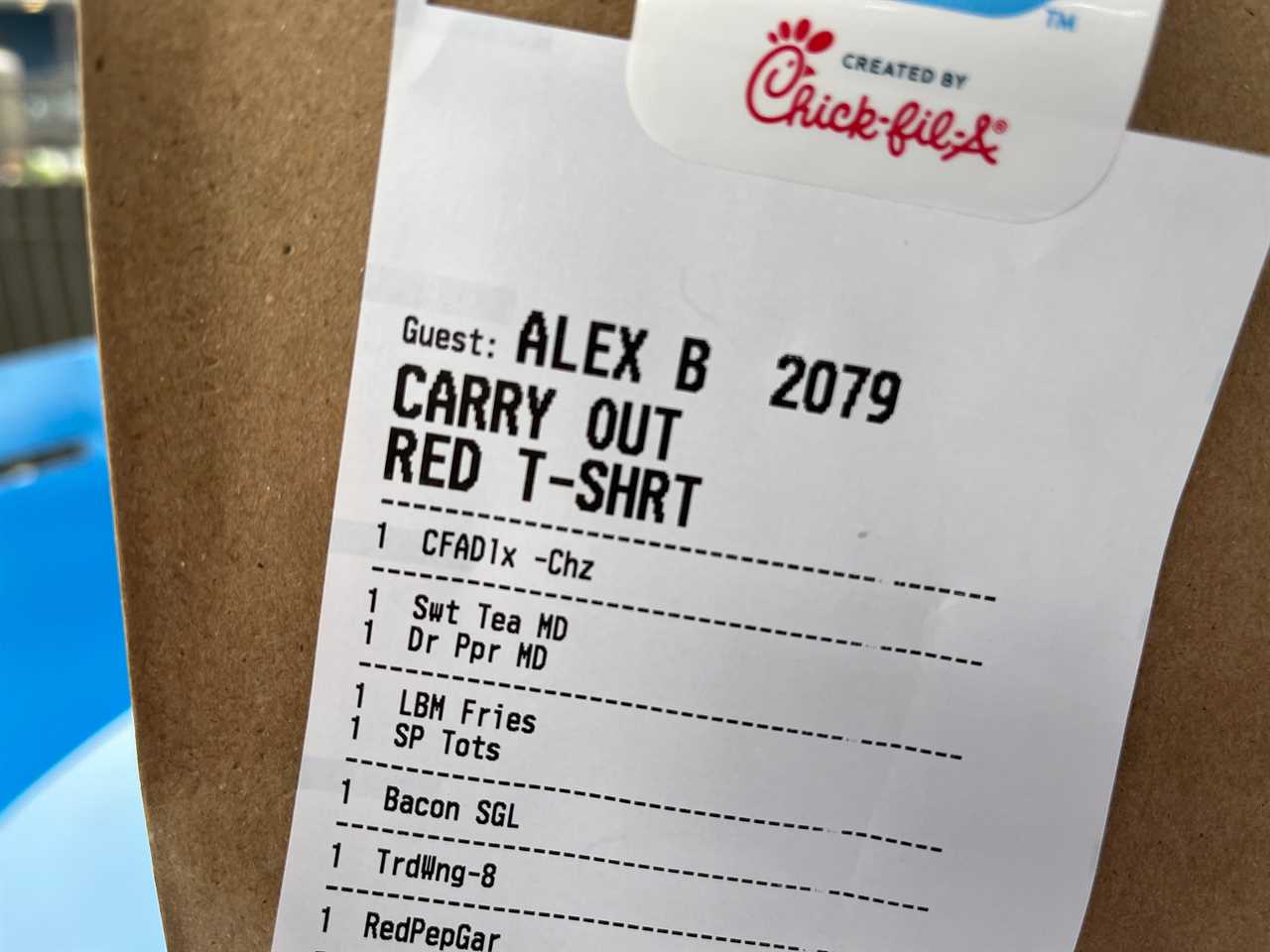 A receipt on the side of a Chick-fil-A bag includes the order's name as well as the fact that they were wearing a red t-shirt when they ordered.