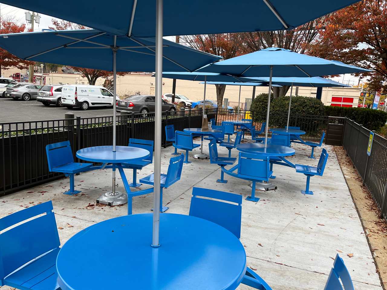 Blue metal tables and chairs with umbrellas above them sit outside a Little Blue Menu location in College Park, Maryland.