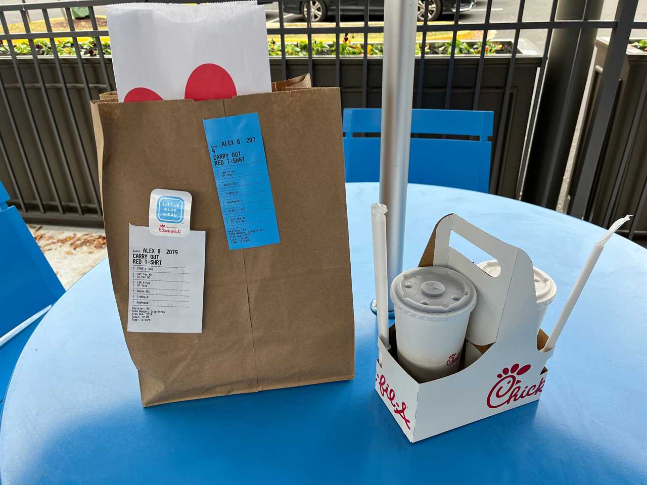 Chick-fil-A drinks in disposable cups and a holder sit on a blue table next to a brown paper bag containing food from the fast food restaurant.