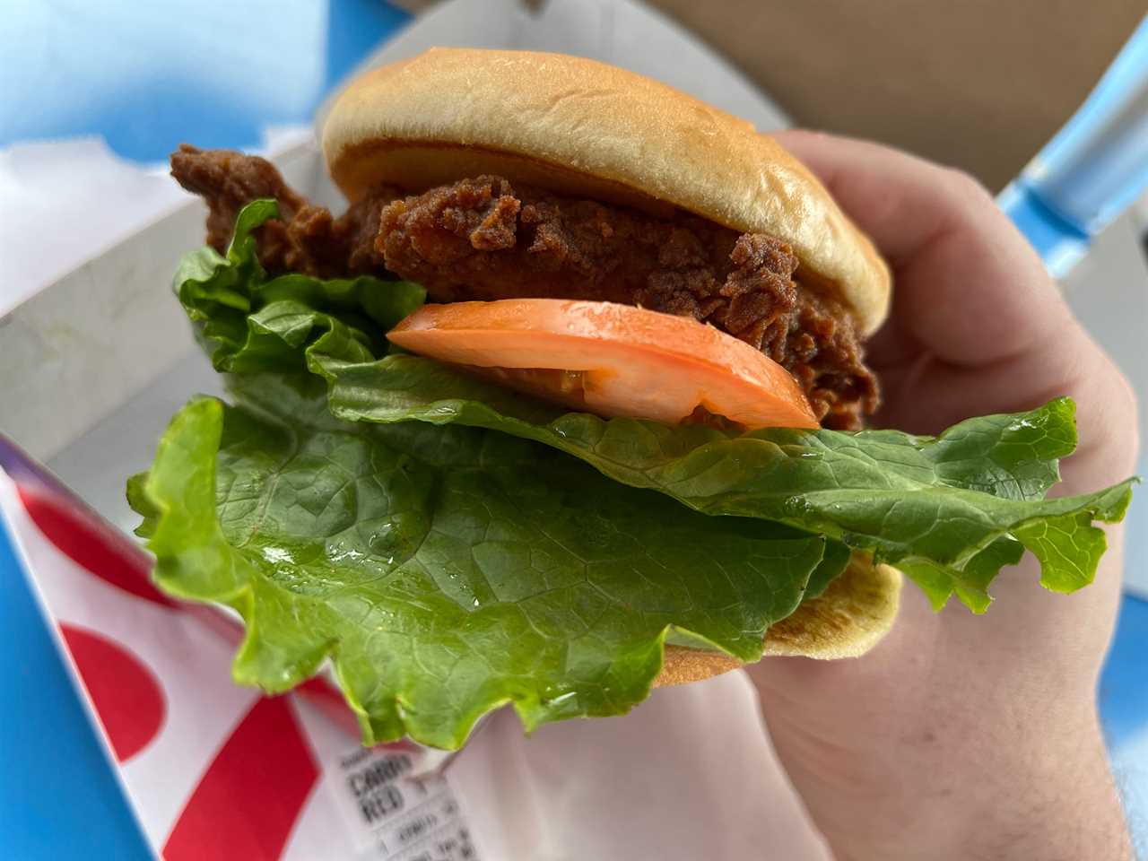 The reporter holds a Chick-fil-A chicken sandwich, including a piece of fried chicken on a bun with lettuce and tomato, at Little Blue Menu