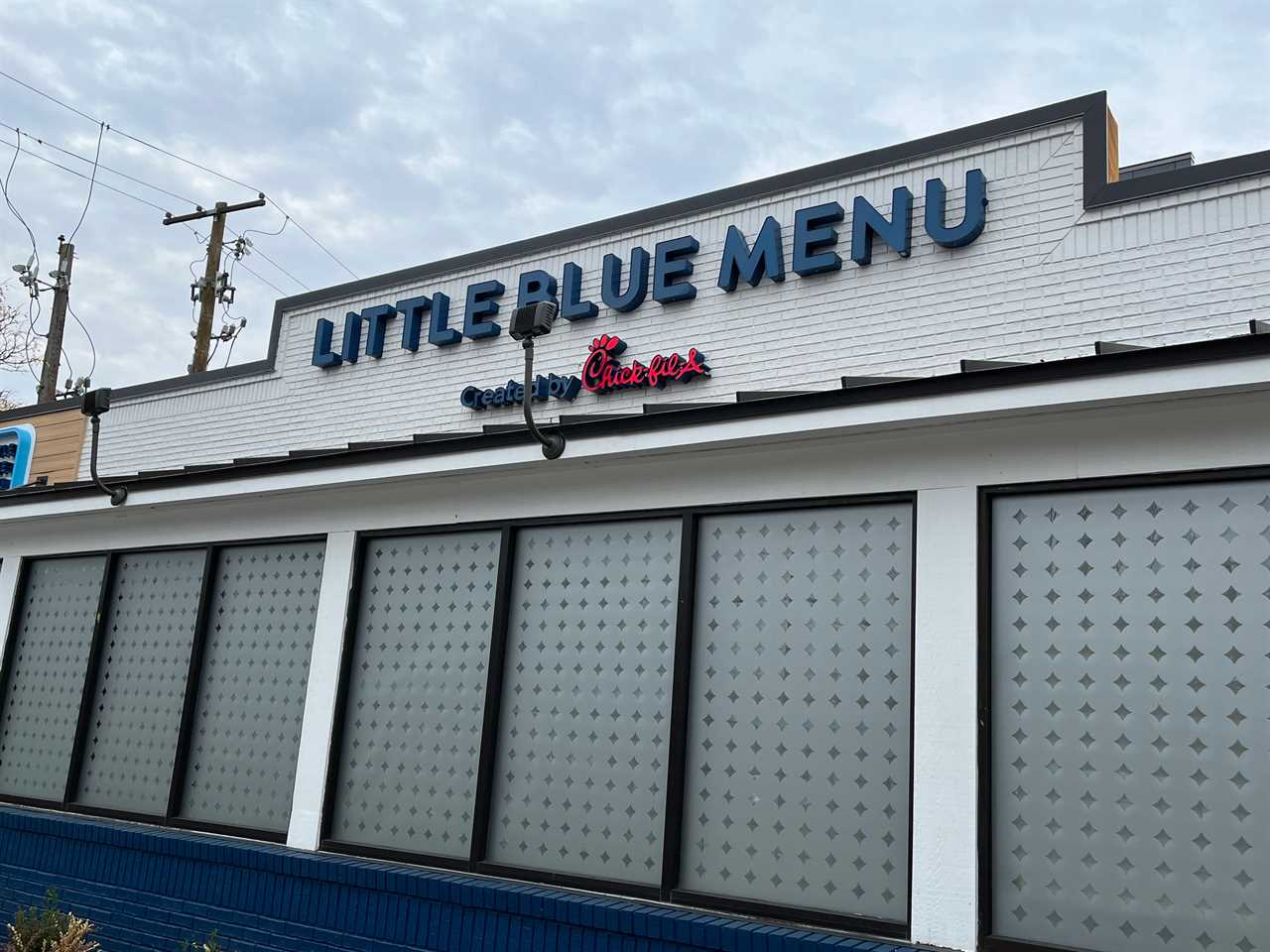 The front of Little Blue Menu, including a blue, all-caps sign and frosted glass windows, in College Park, Maryland.