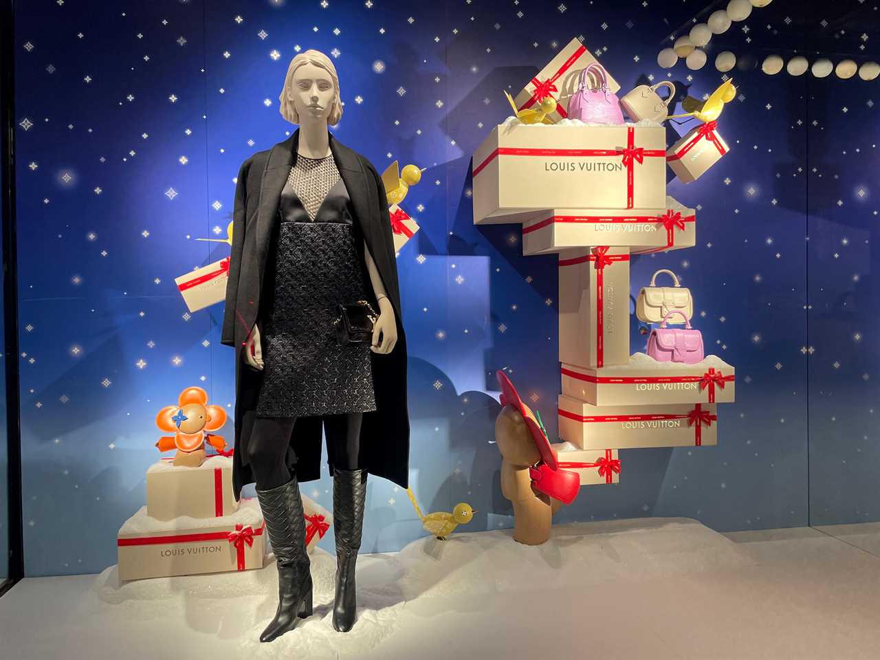 the holiday window at Louis Vuitton shows a mannequin wearing black and sculptures of gifts stacked