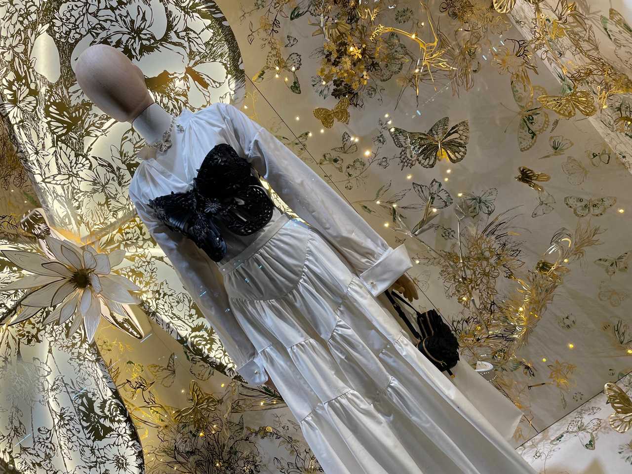 a mannequin wears white dress in front of sparkly background in Dior window display