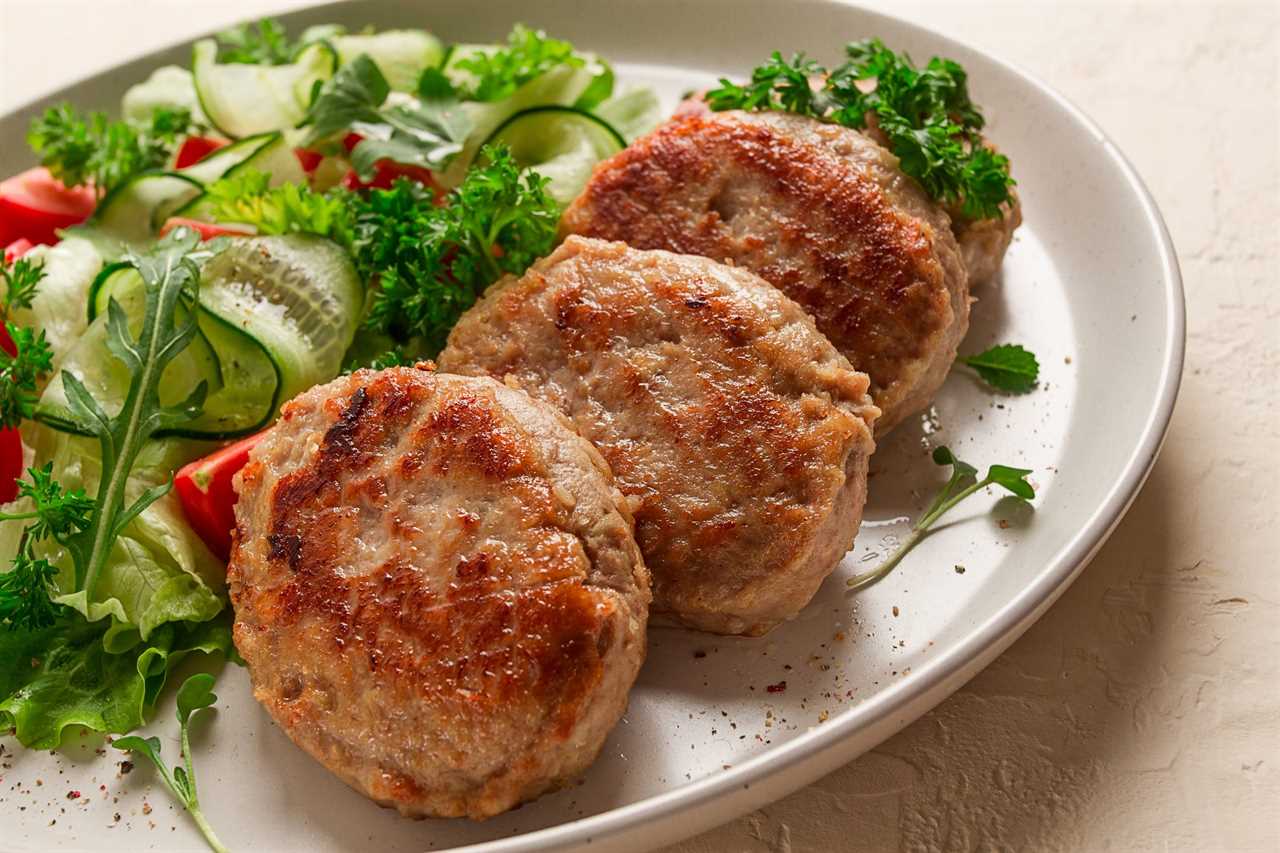 A plate of three turkey burger patties next to a mixed green salad.