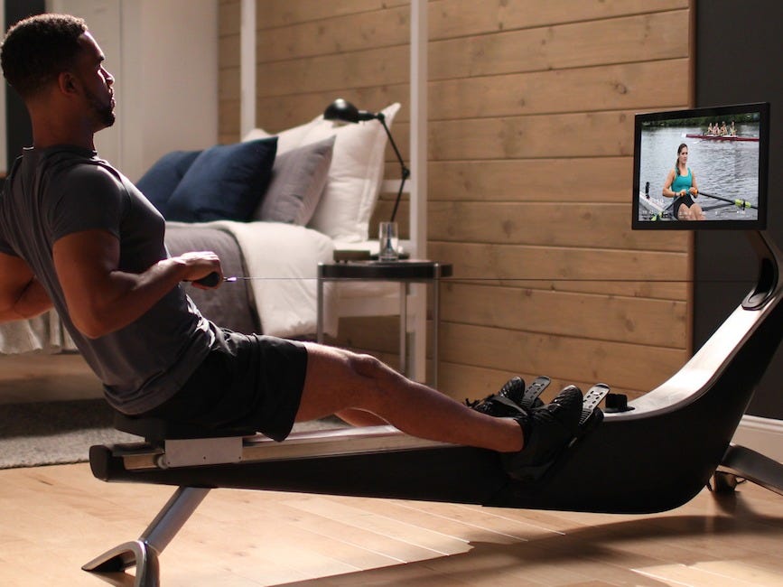 a model uses the Hydrow Rowing Machine in a room with wood-planked walls.