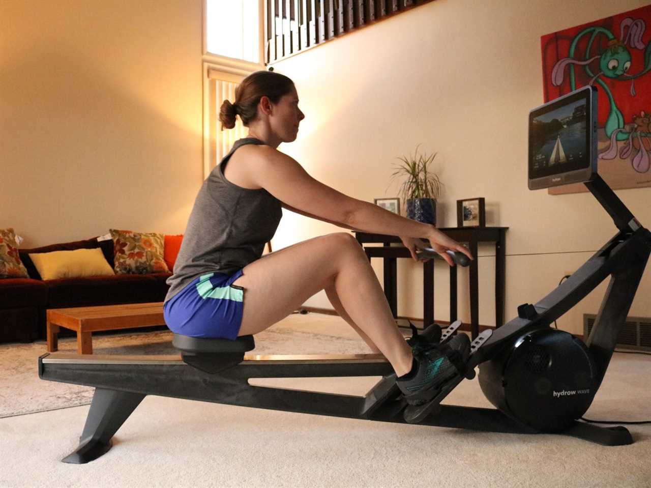 person using a Hydrow Wave rowing machine in a living room.