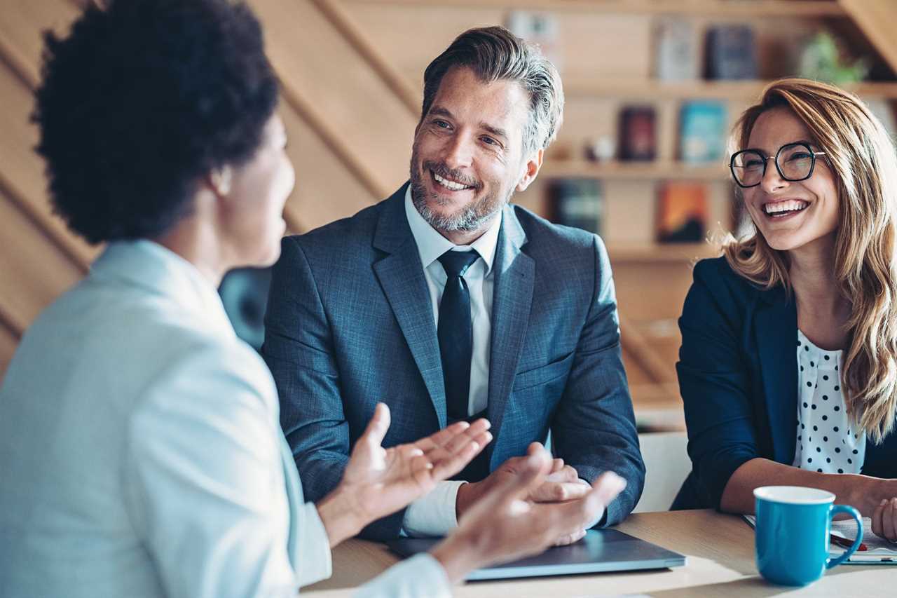 Three wealth managers in professional clothes sitting at a table and talking.