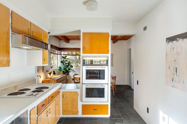 The light-filled kitchen offers a striking blend of old and new, featuring vintage appliances and original cabinetry. A pass-through opening connects the space with the dining area.