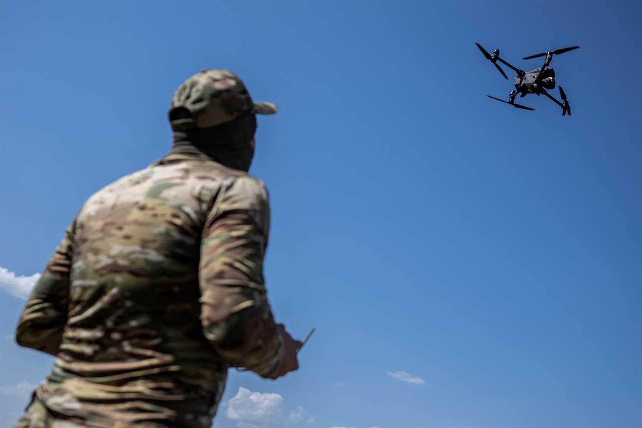 A man holds a remote control and looks up at a drone in the sky.