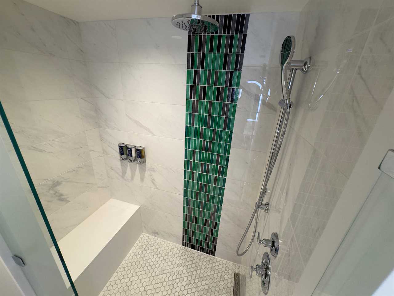 Walk-in rain shower with green tiles and white tiles and a bench inside at Disneyland Hotel villa