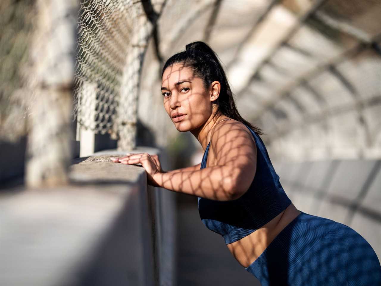 A woman in fitness clothing leans against a wall.