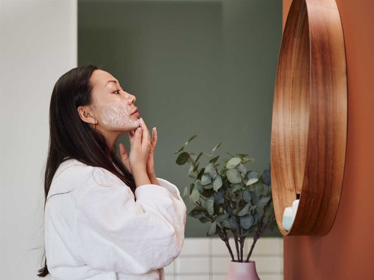 A woman puts cream on in the mirror.