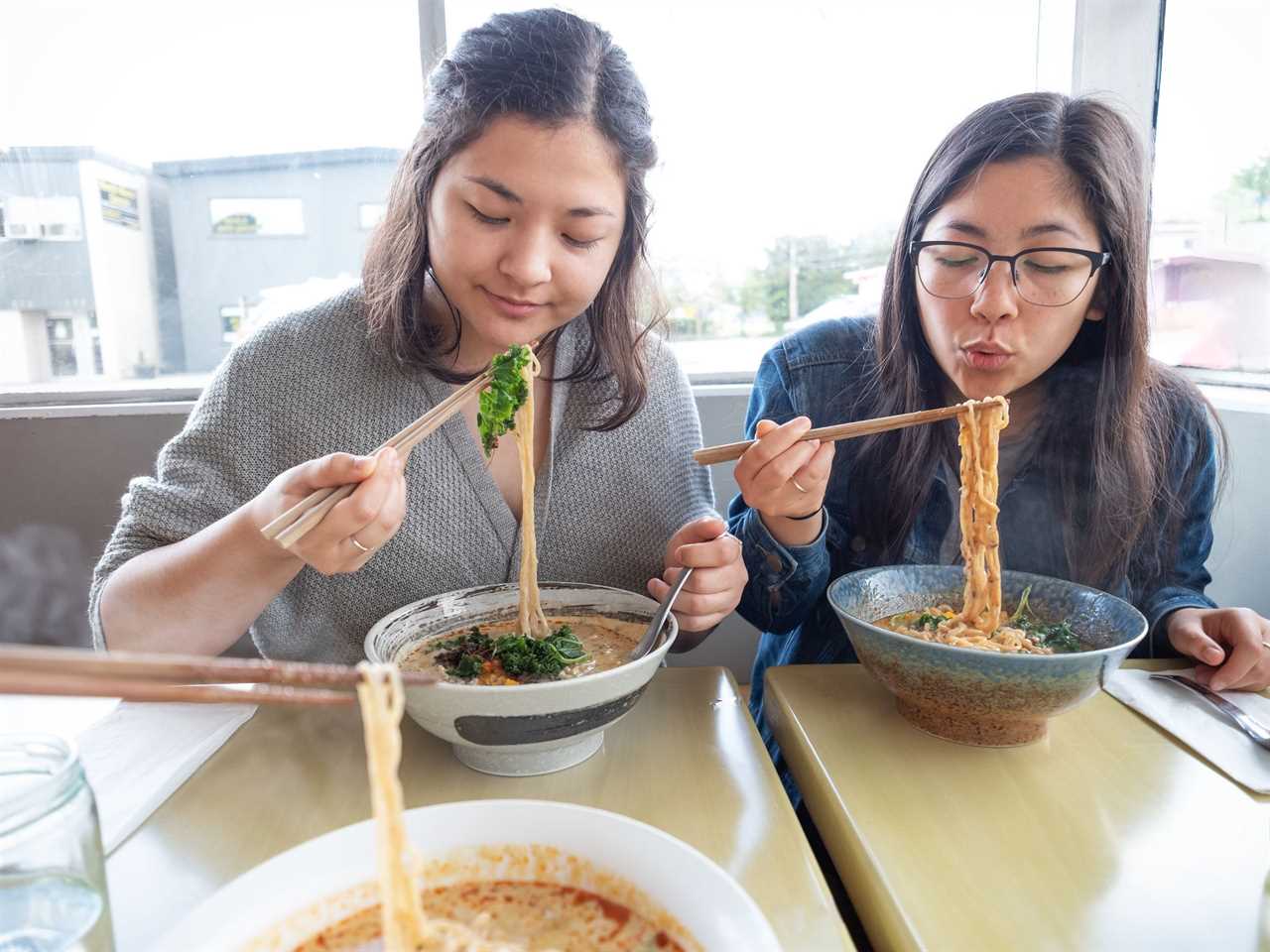 Women eat noodles from bowls.