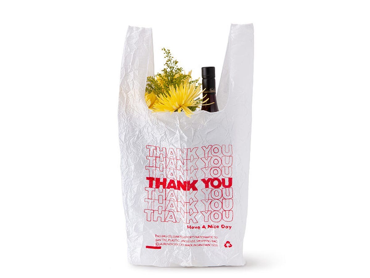 tote bag embroidered with repeated "Thank You" text to look like a takeout bag holding flowers and a bottle of wine.