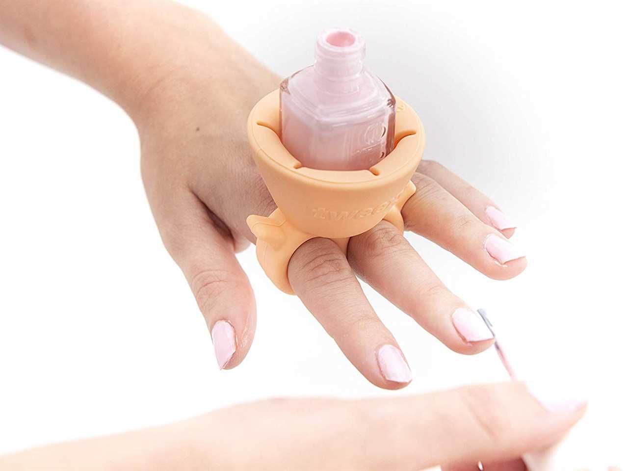 Person's painting their nails while wearing a ring nail polish bottle holder to hold their polish.