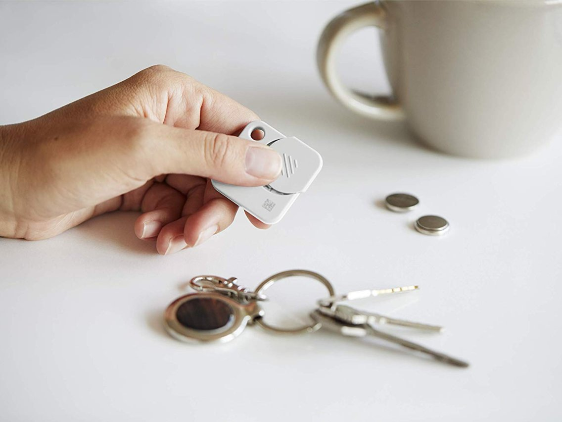 Person holding a Tile Mate bluetooth tracker next to a set of keys with a tracker attached to the keyring.