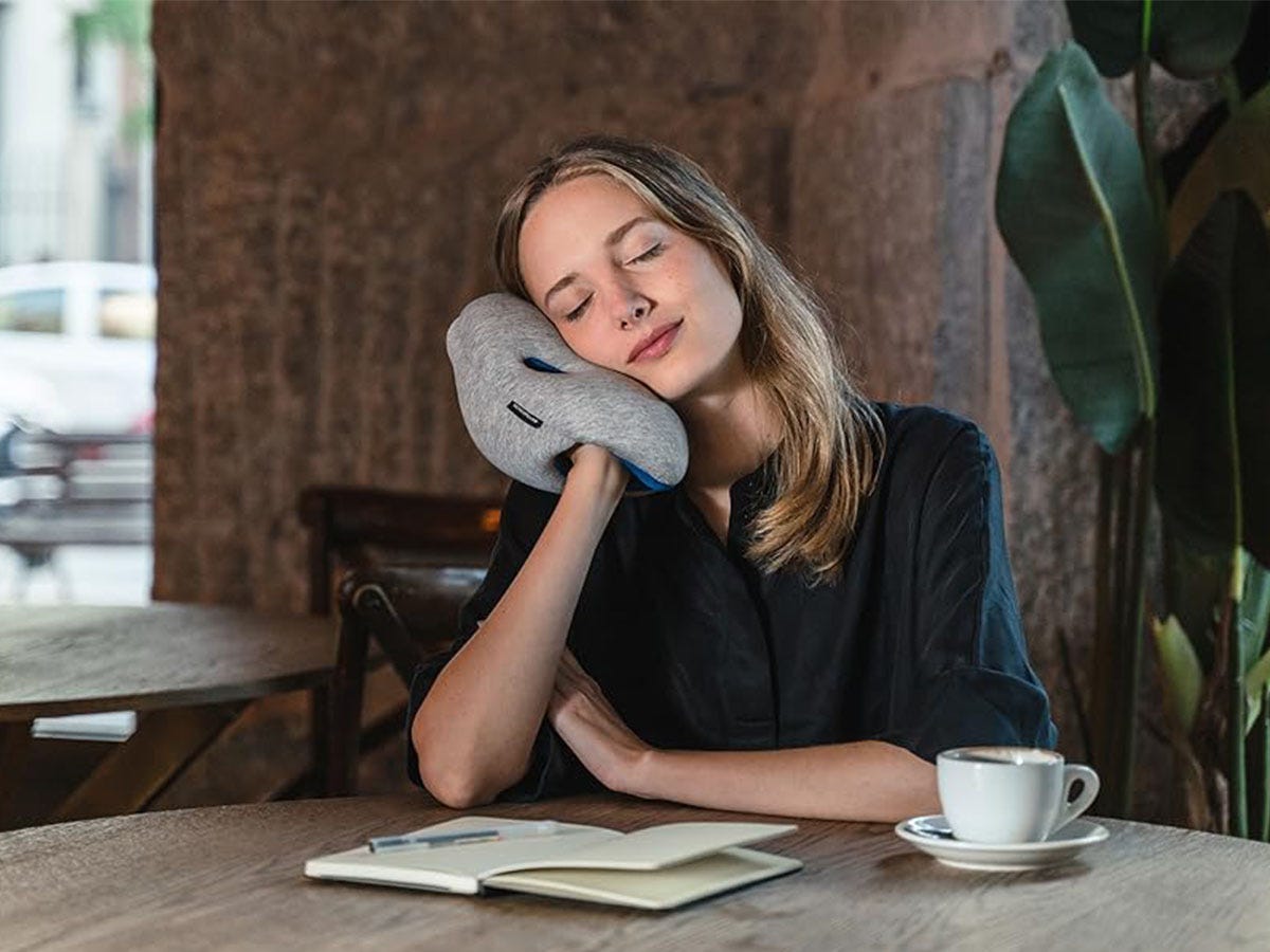 A woman sitting at a breakfast table holding a mini Ostritchpillow over her shoulder.